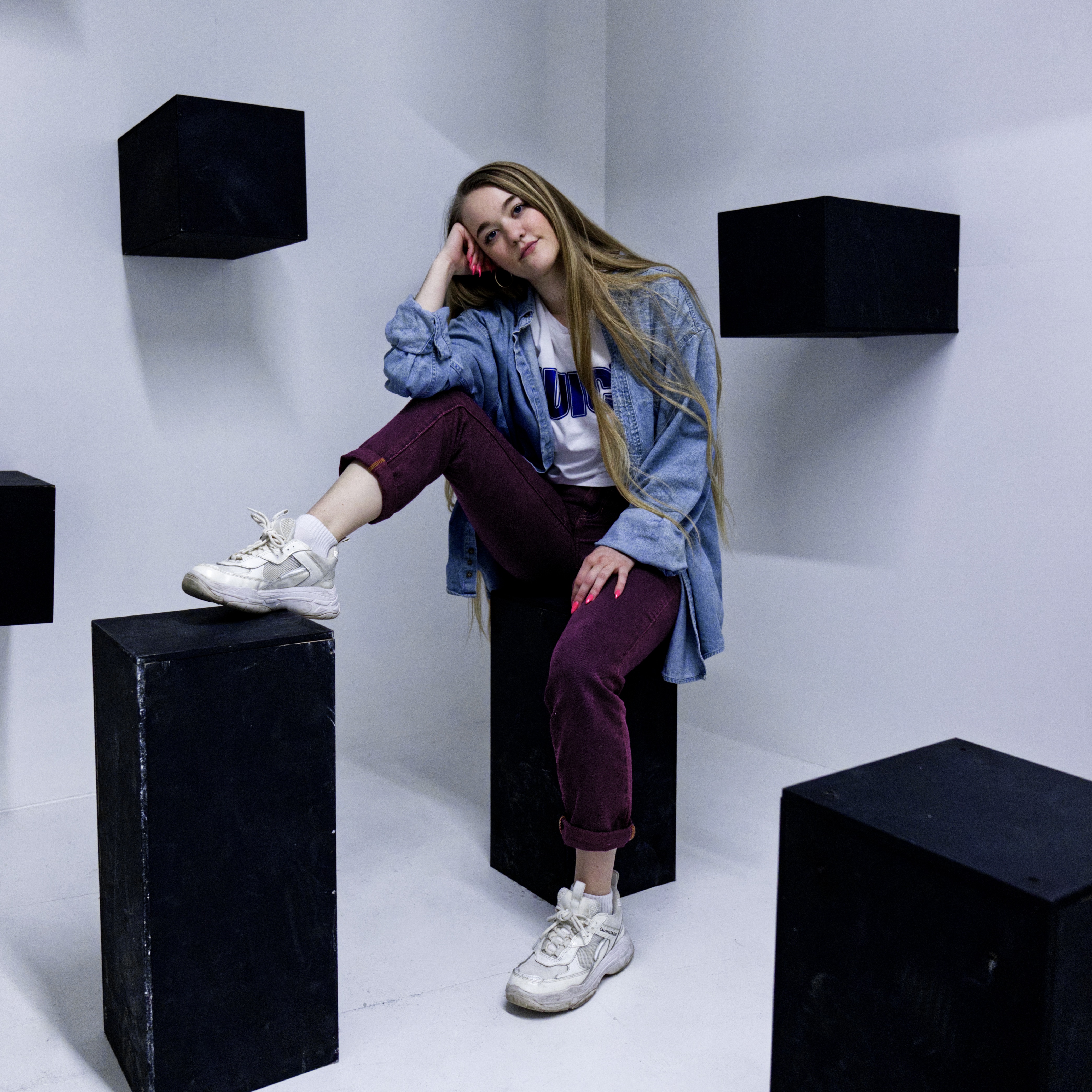 girl posing in the midst of a bunch of black boxes with a white wall